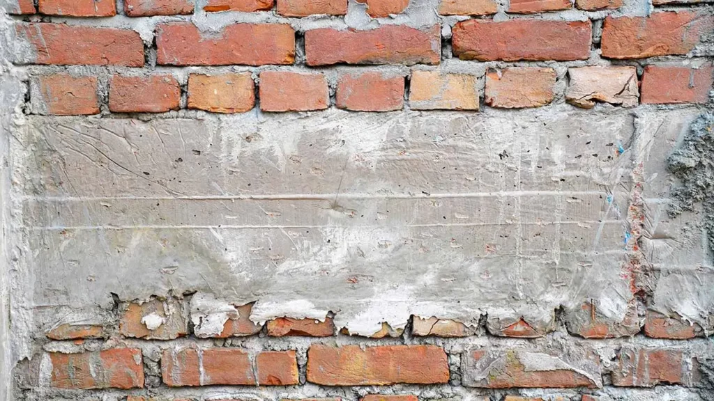 A red brick wall partially covered in a rough layer of gray cement, creating a contrast between the textured bricks and the smooth plaster.